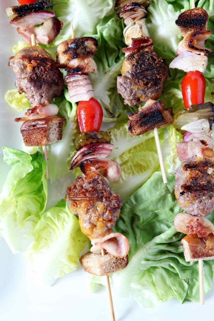 Close up of cooked deconstructed burger bites on skewers, laid out on lettuce