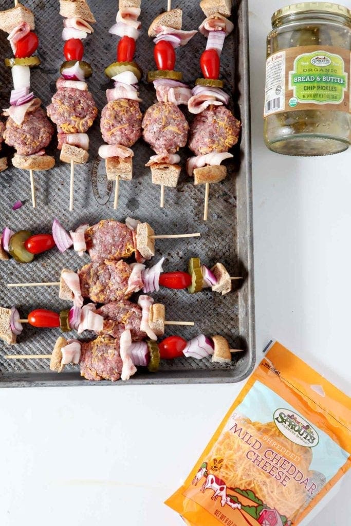 Prepared burger bites on kebab skewers are laid out on a baking sheet, surrounded by Sprouts ingredients