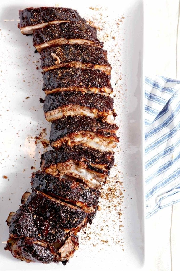 Sliced and seasoned Memphis-Style Barbecue Ribs on a white platter, set on top of a blue and white striped towel before serving