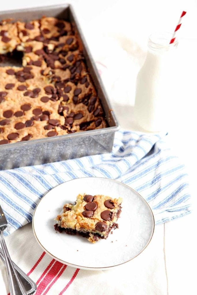 A cheesecake brownie sits on a white plate next to a tray