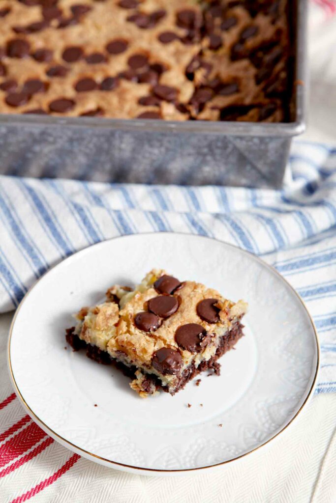 A cheesecake brownie on a white plate by a pan of the dessert