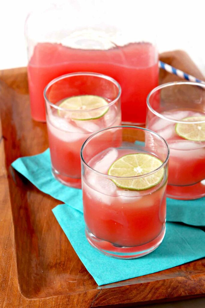 Three glasses of Spiked Watermelon Limeade are served on a platter with a pitcher