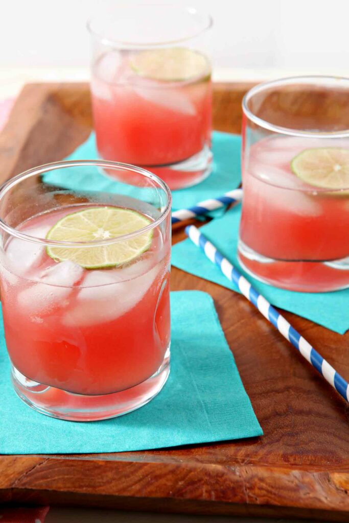 Three glasses of Spiked Watermelon Limeade are served on a wooden platter.