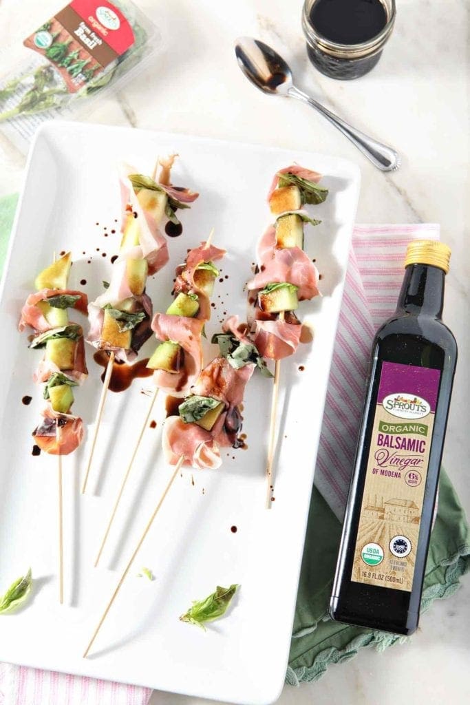 melon skewers on a plate with a bottle of balsamic