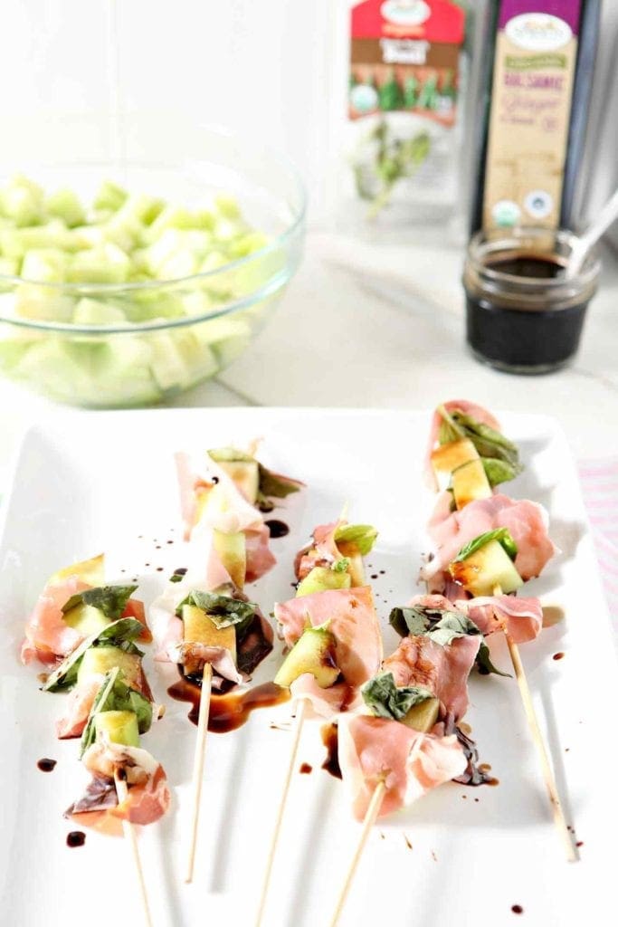 melon skewers on a white plate with ingredients behind