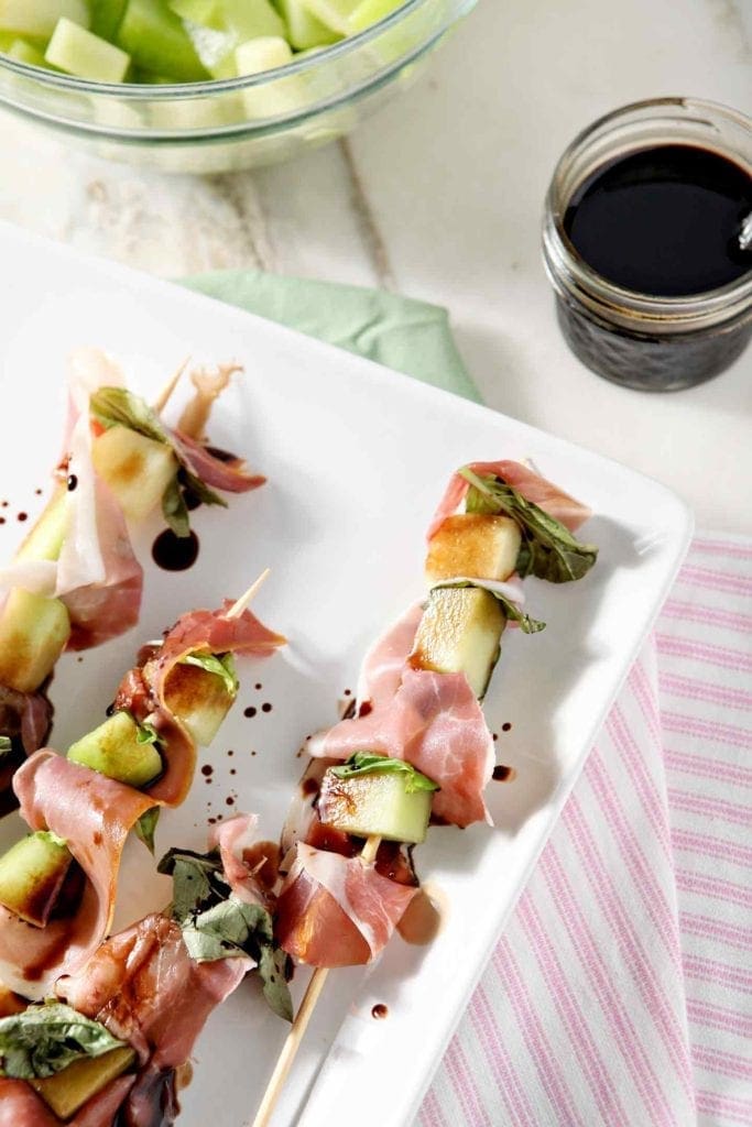 Skewers of prosciutto and melon on white serving dish   