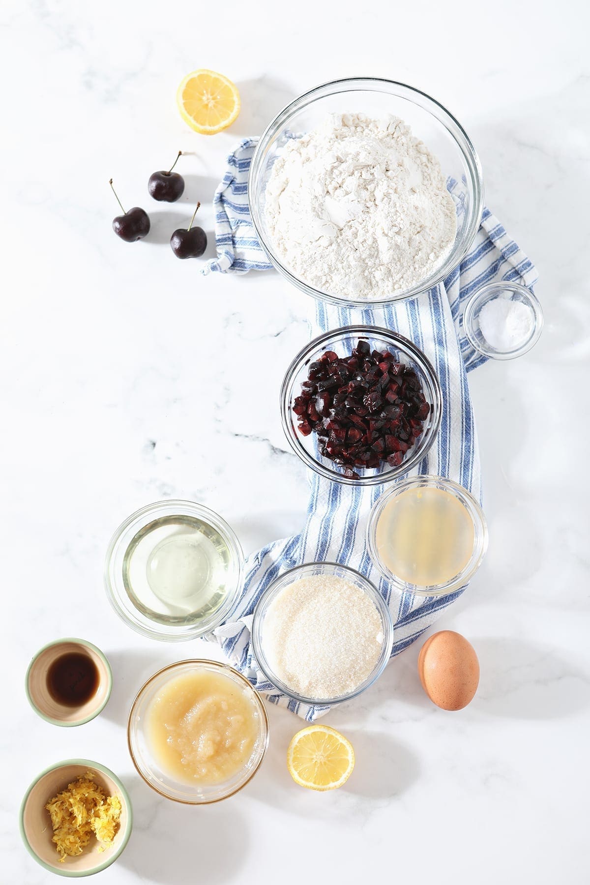 Ingredients for the cherry bread in bowls on top of a blue striped towel on marble