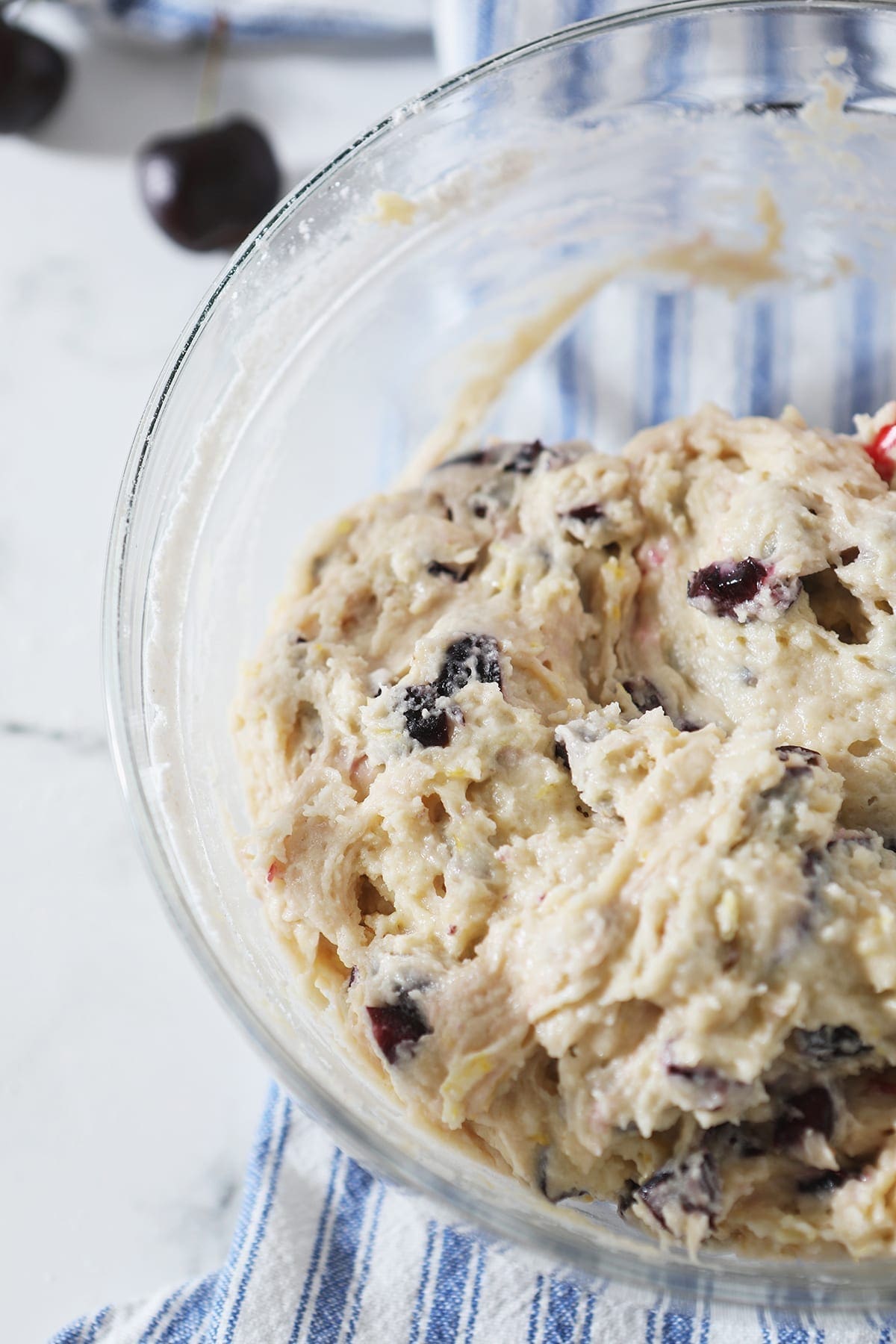 Cherry Bread batter in a clear glass bowl on top of a blue and white striped towel