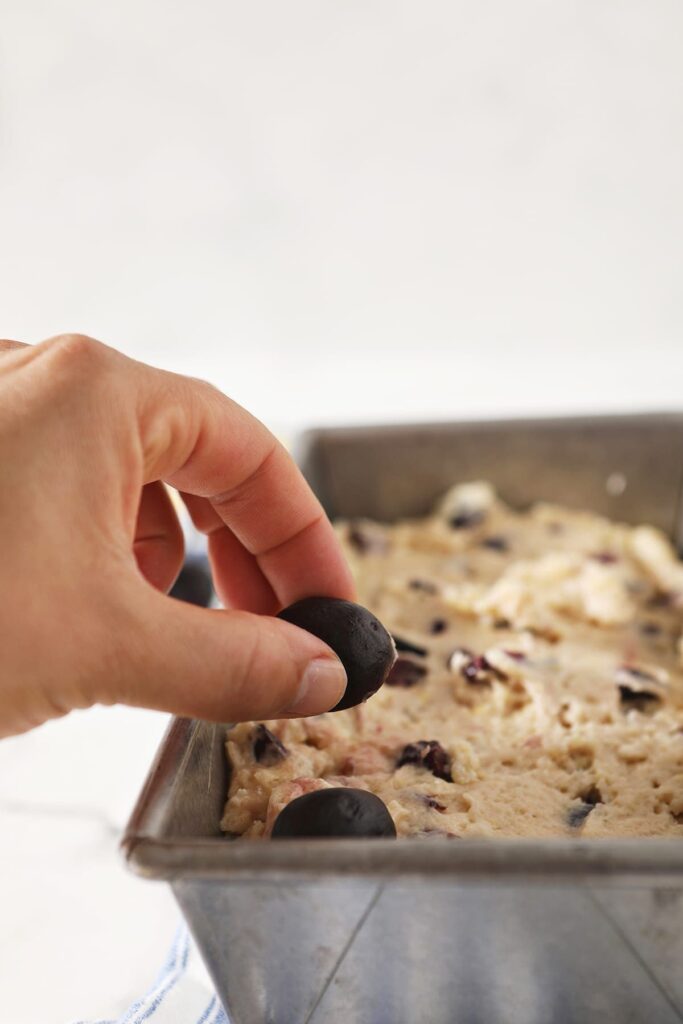 Halved cherries are placed on top of bread dough in a metal bread tin