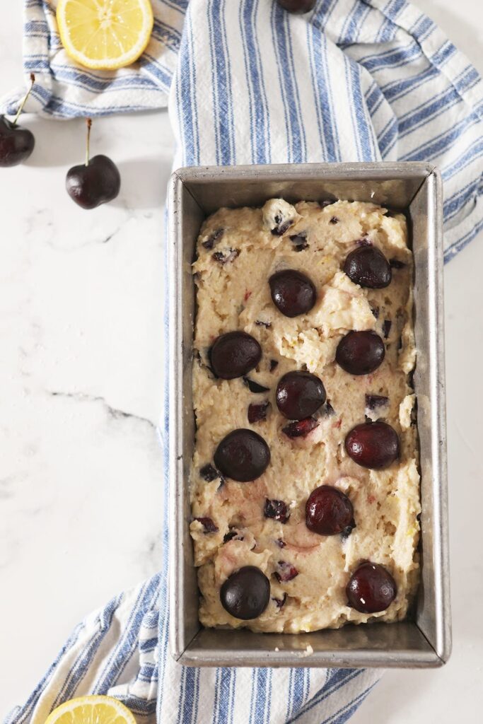 Batter for Cherry Quick Bread in a metal tin on top of a blue and white striped towel before baking