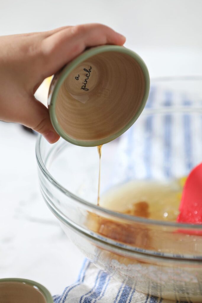 Vanilla pours into a glass bowl holding wet ingredients for bread