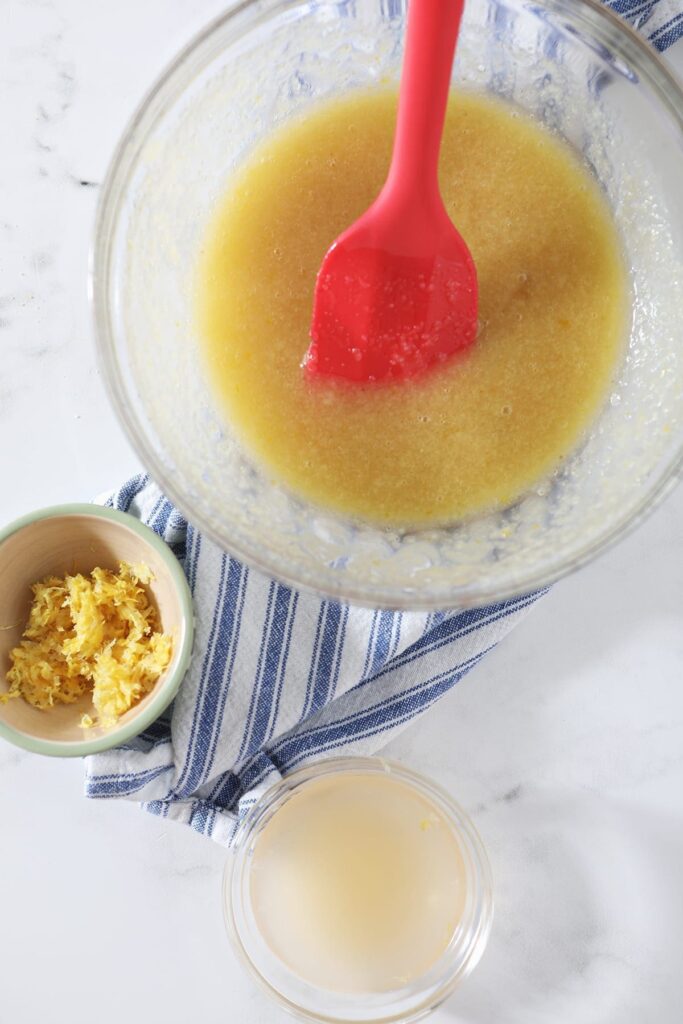 Wet ingredients in a bowl with lemon zest and juice on top of a blue and white striped towel