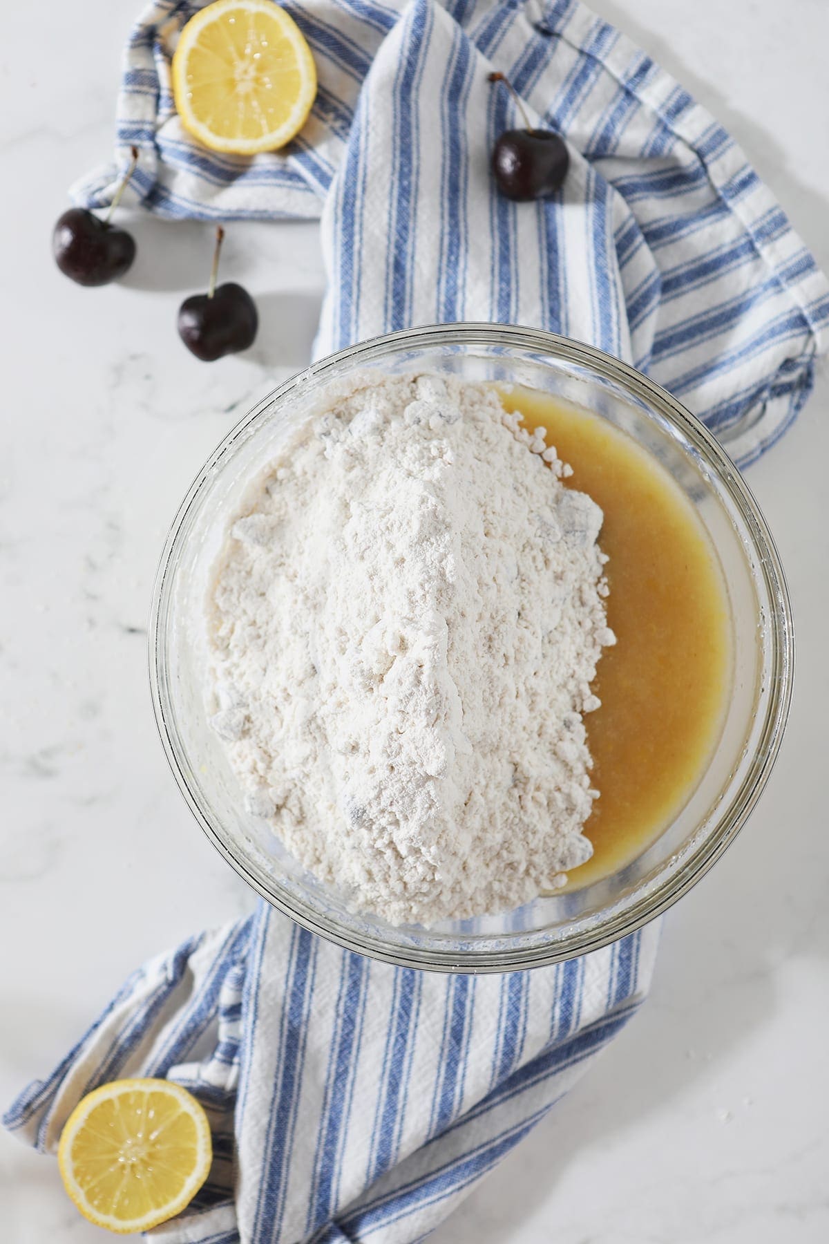 Dry ingredients on top of wet ingredients in a clear glass bowl on top of a blue and white striped towel