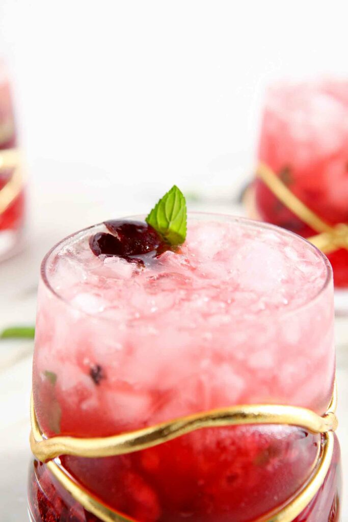 Close up of a cherry drink with crushed ice and a cherry and mint garnish