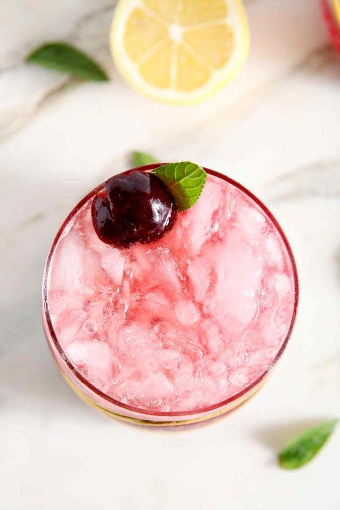 A pink drink garnished by a cherry and a sprig of mint