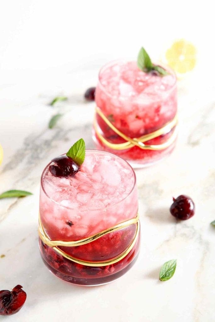 Two cherry vodka drinks on marble with cherries and mint