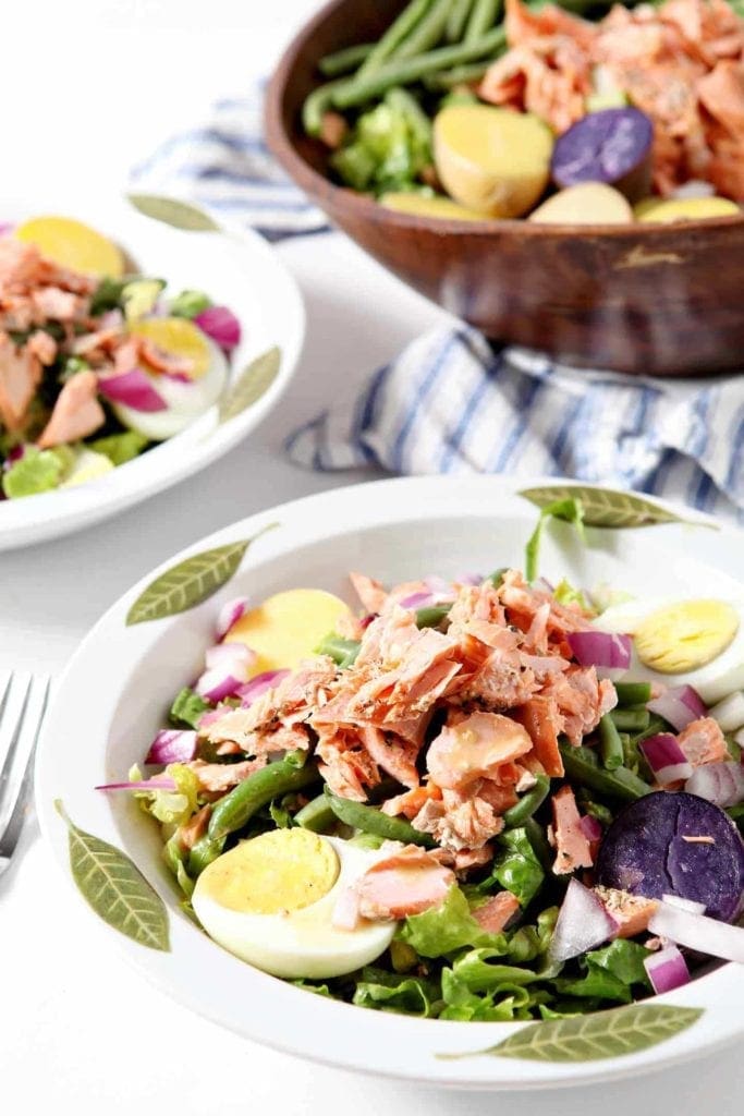 salmon nicoise salad in two white bowls with green leaves