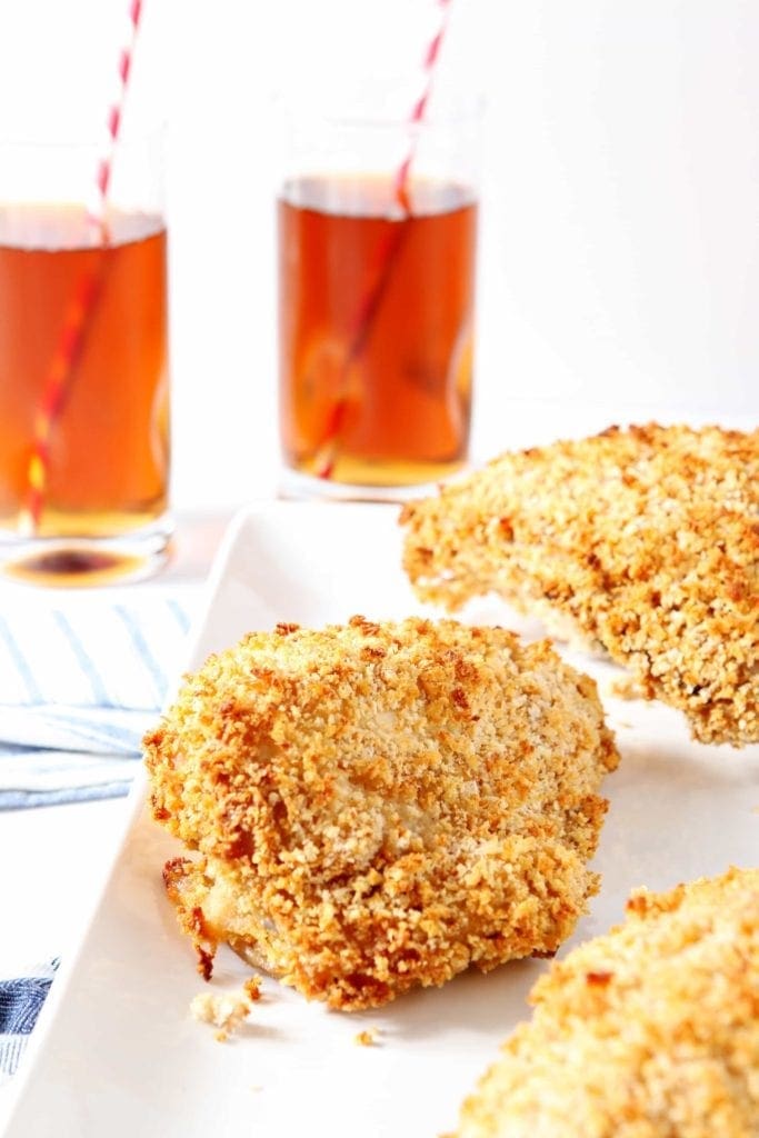 two pieces of oven fried chicken on a white plate and tea in the background