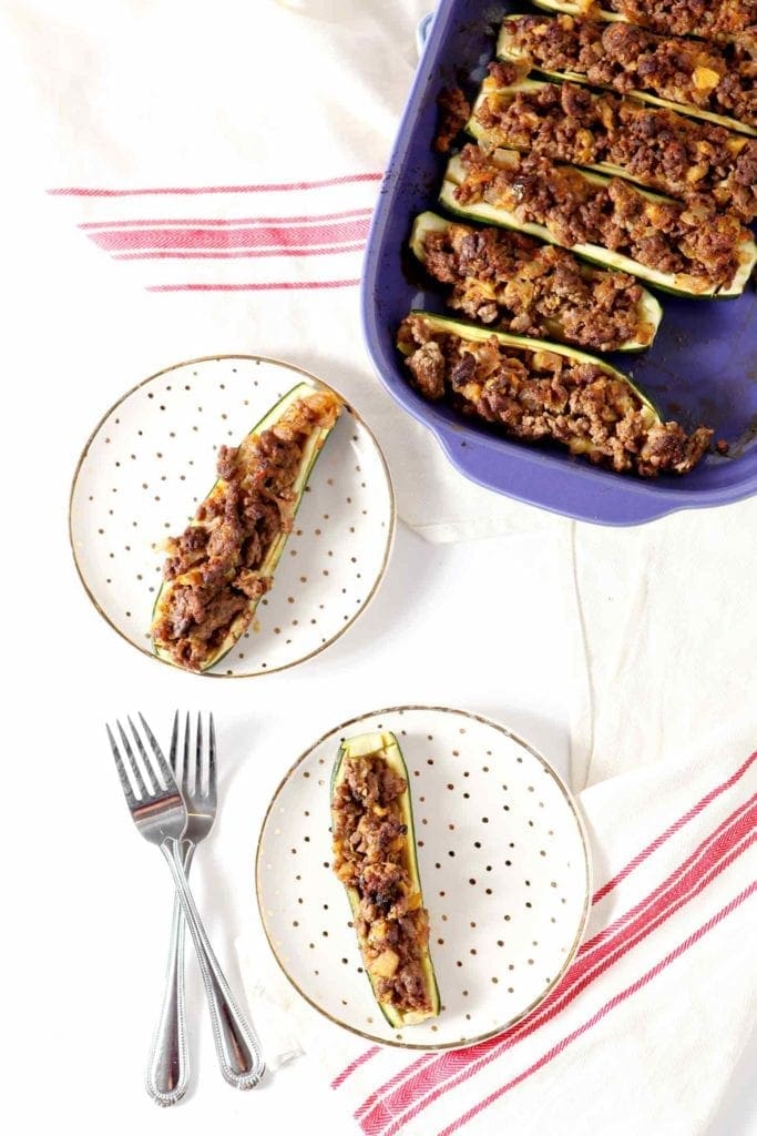 Whole30 Taco Zucchini Boats served on gold flecked plates with the baking dish of other zucchini on a white background