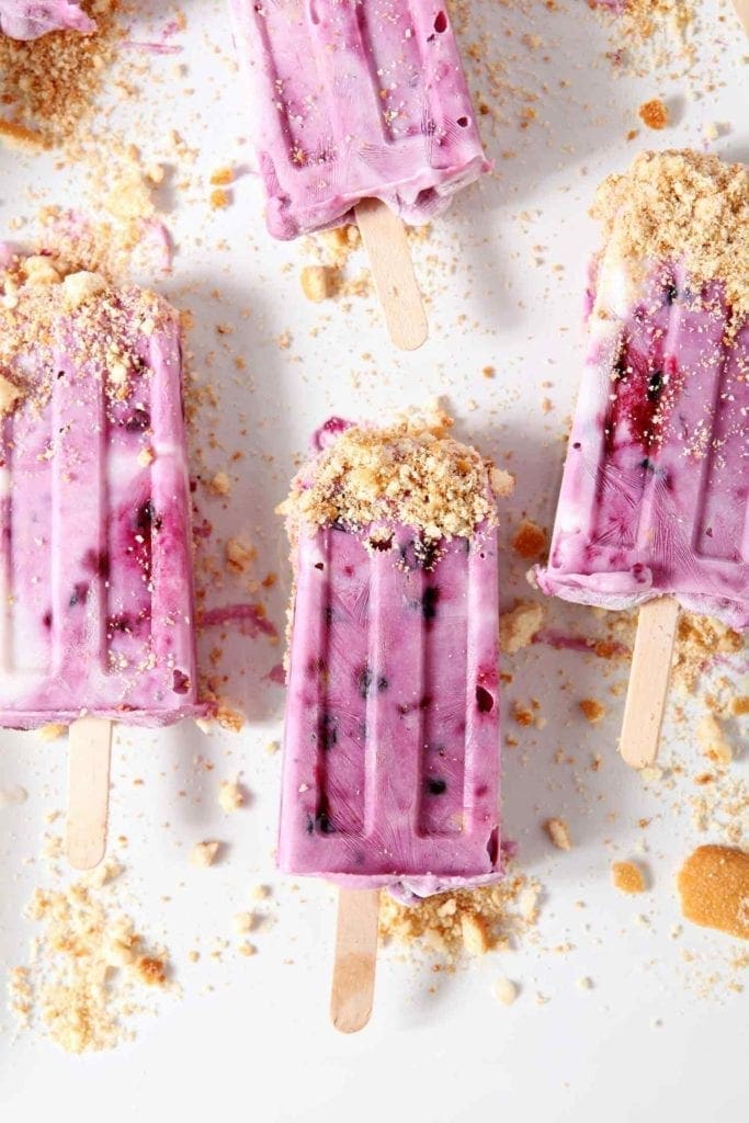 Several Blueberry Cheesecake Popsicles, dipped in graham cracker crumbs, are displayed on a white platter before eating.