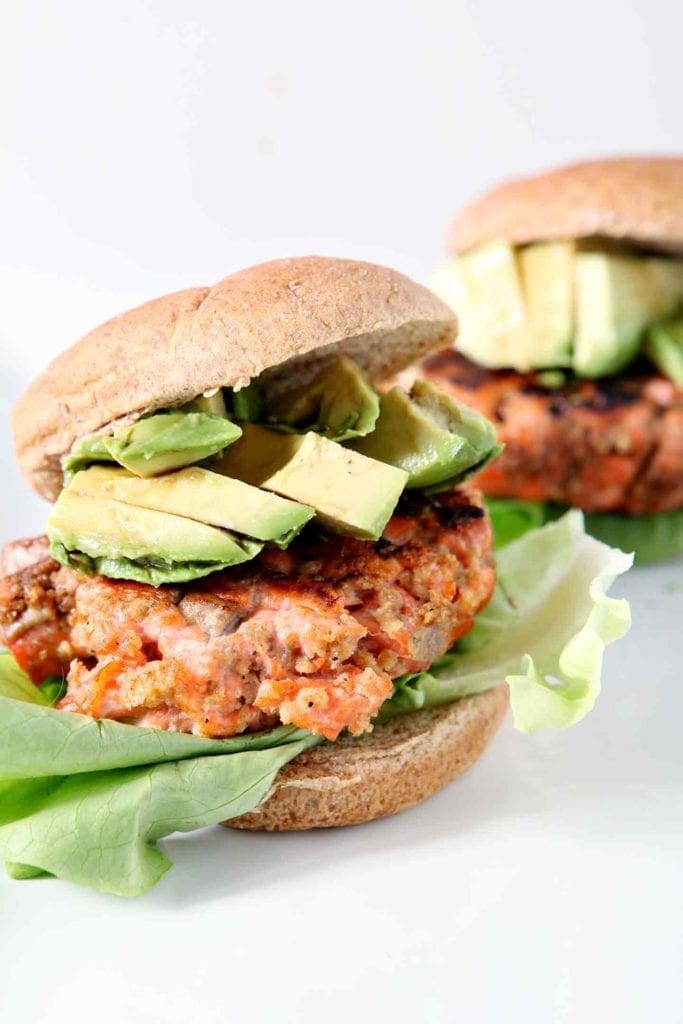 Two Classic Salmon Burgers are shown, dressed with lettuce and avocado, on whole wheat buns.