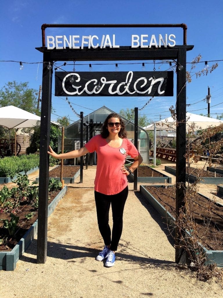 Woman standing under beneficial beans garden sign 