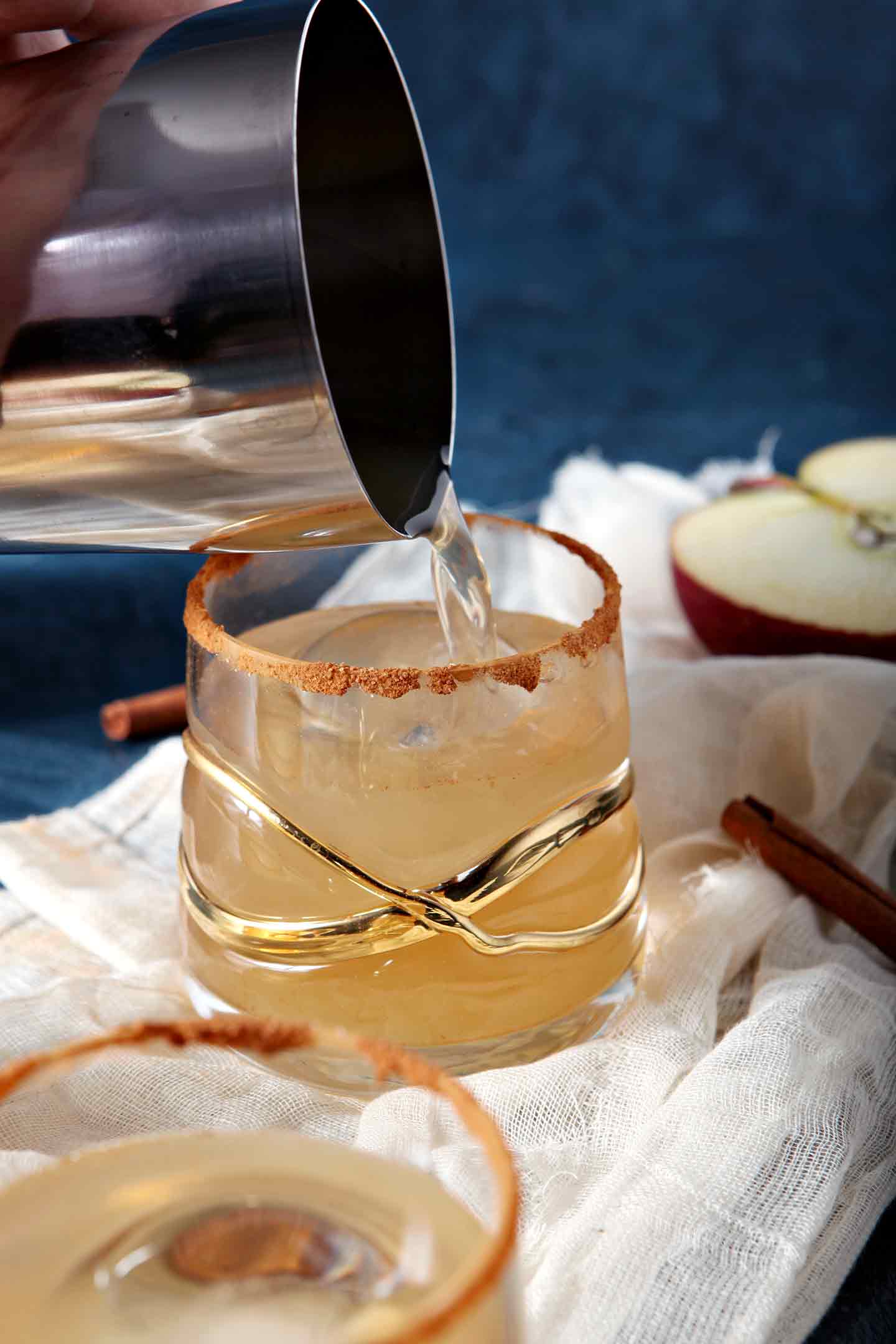 A cocktail shaker pours a drink into prepared old fashioned glass with gold garnishes