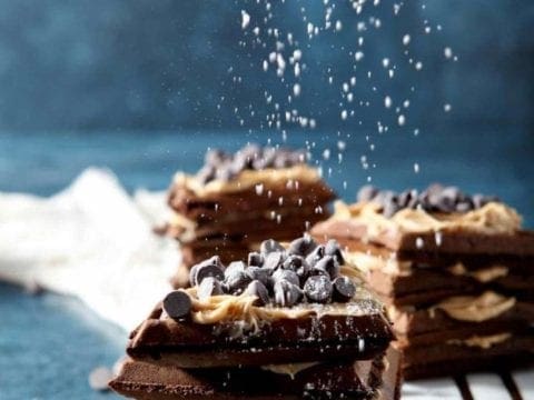 dusting powdered sugar on a peanut butter chocolate waffle sandwich