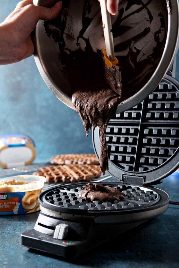 pouring chocolate waffle batter in a waffle maker