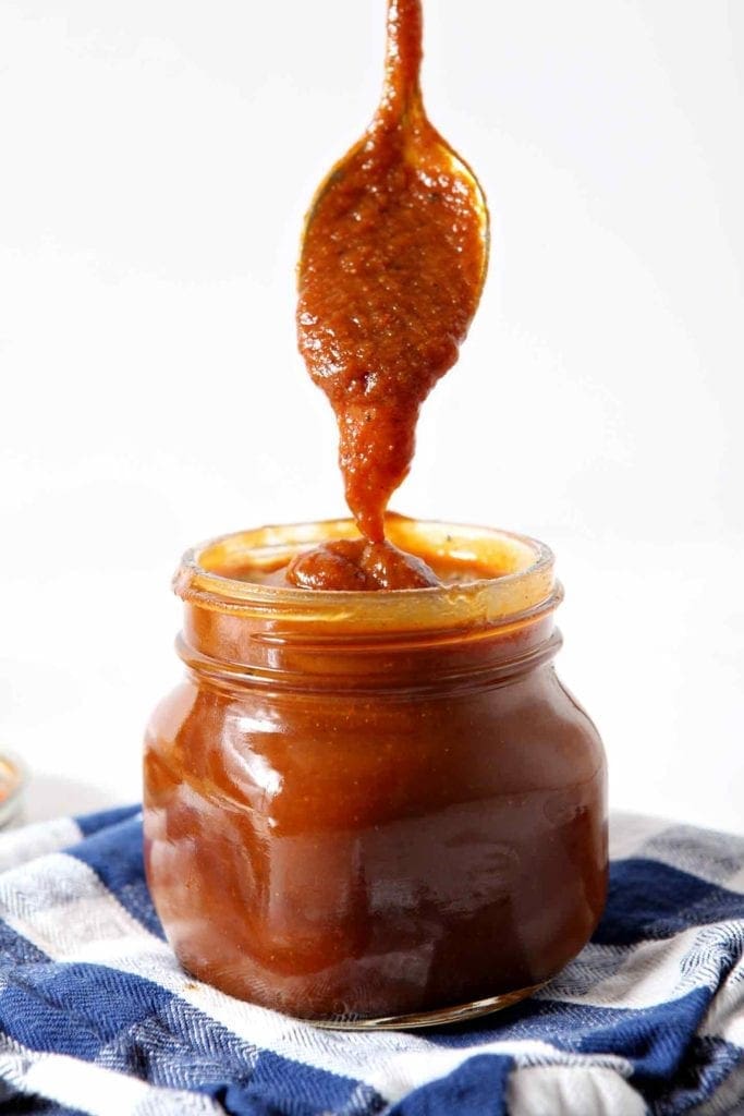 A spoon drizzles Pumpkin Barbecue Sauce into a mason jar