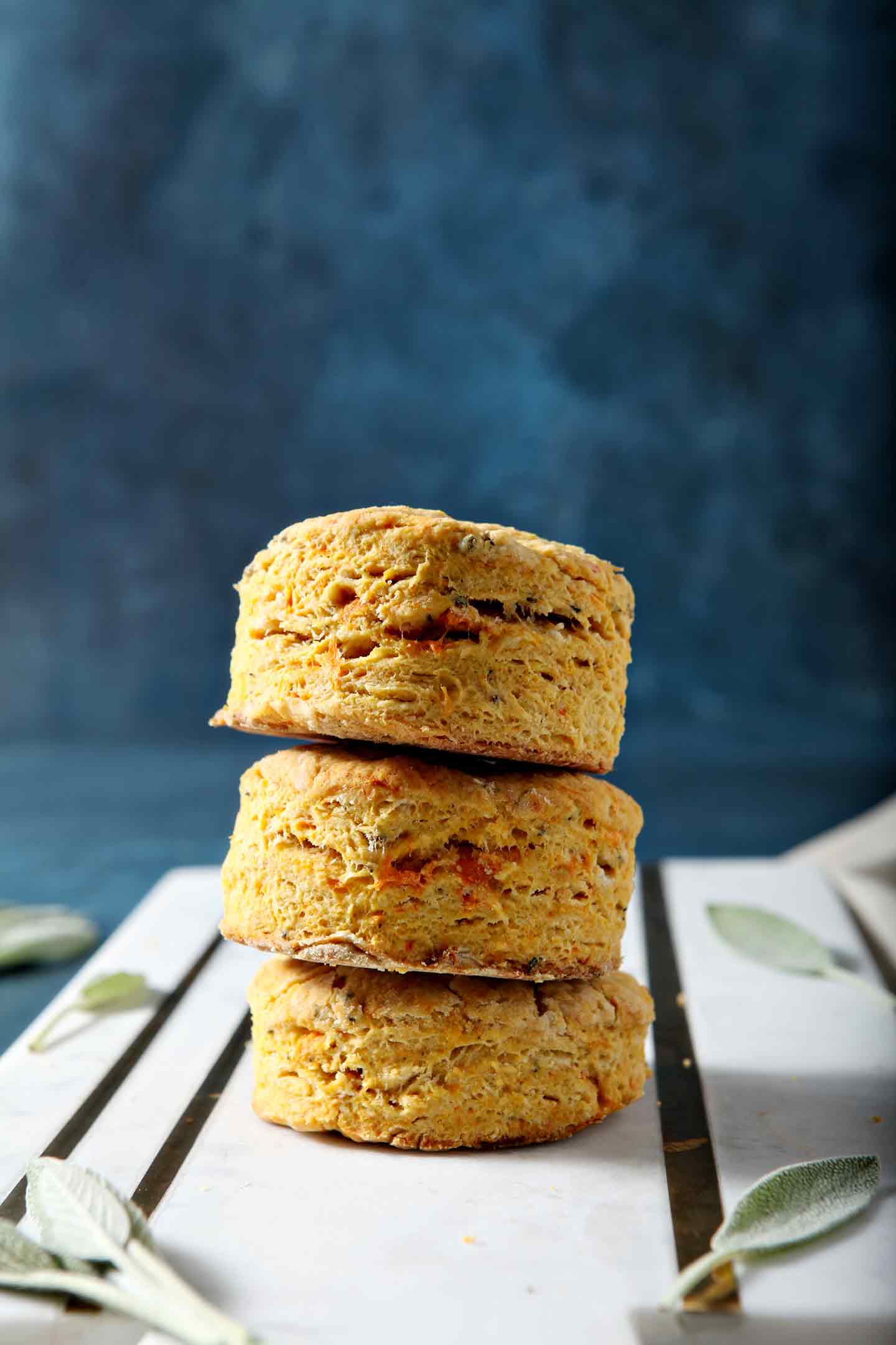 Bake Sage Sweet Potato Olive Oil Biscuits are stacked on top of one another on a marble serving platter