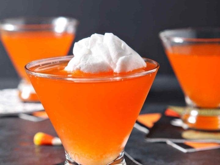 Three bright orange Candy Corn Martinis sit on a black background