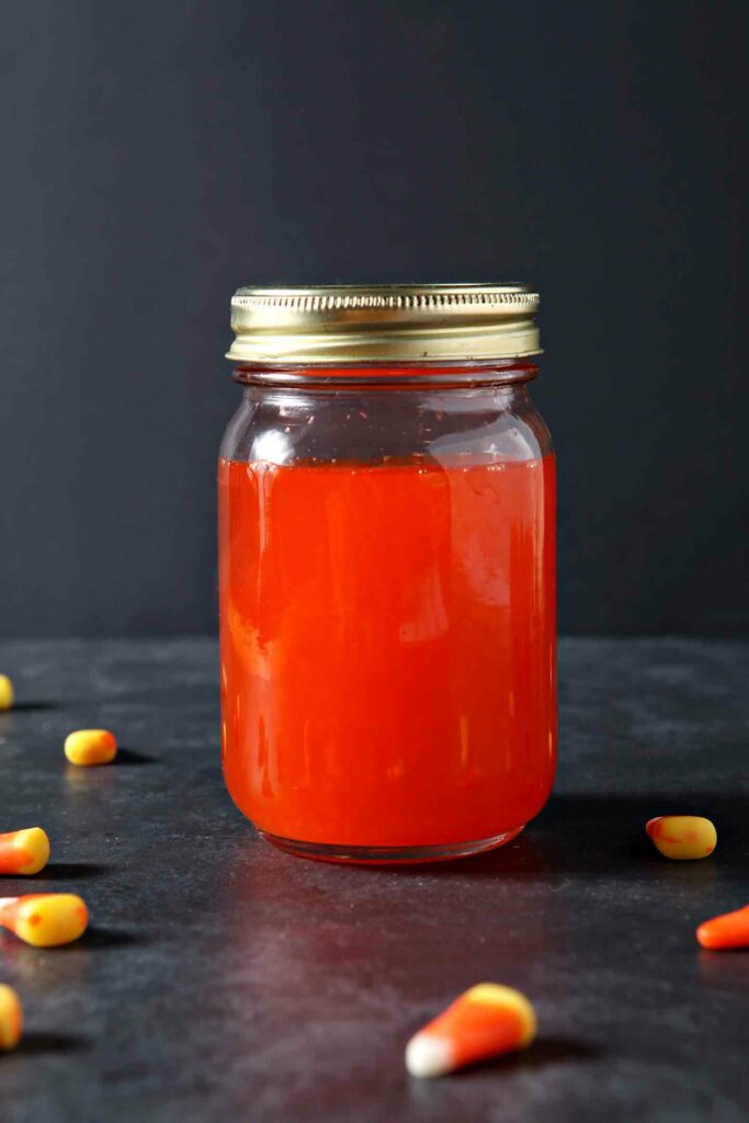 Candy corn vodka, in a mason jar, surrounded by candy corn