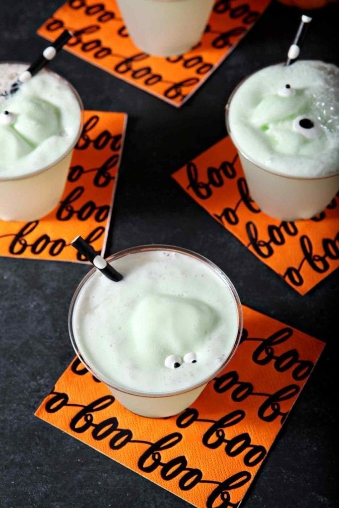 Four glasses of a Halloween drink for kids are displayed on orange napkins on a black background