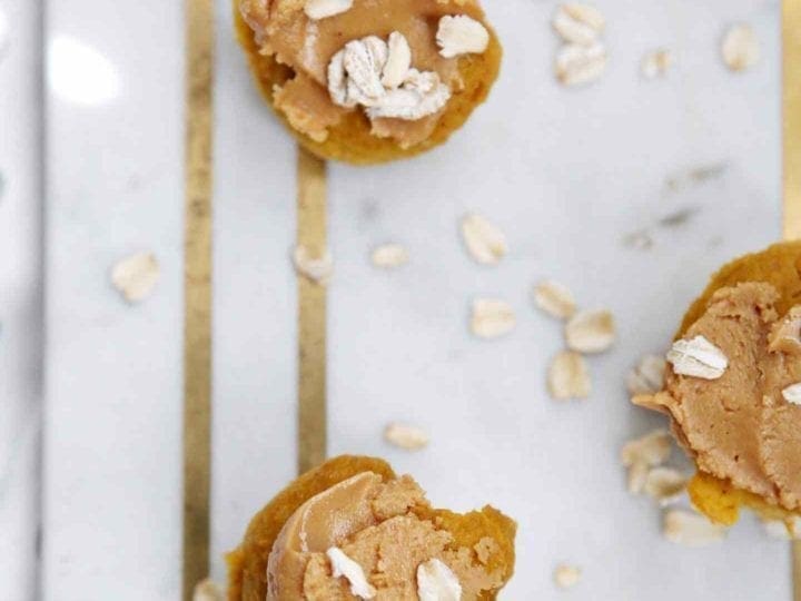 Overhead of homemade pupcake recipe, frosted with extra peanut butter, on a marble slab with oats sprinkled around them