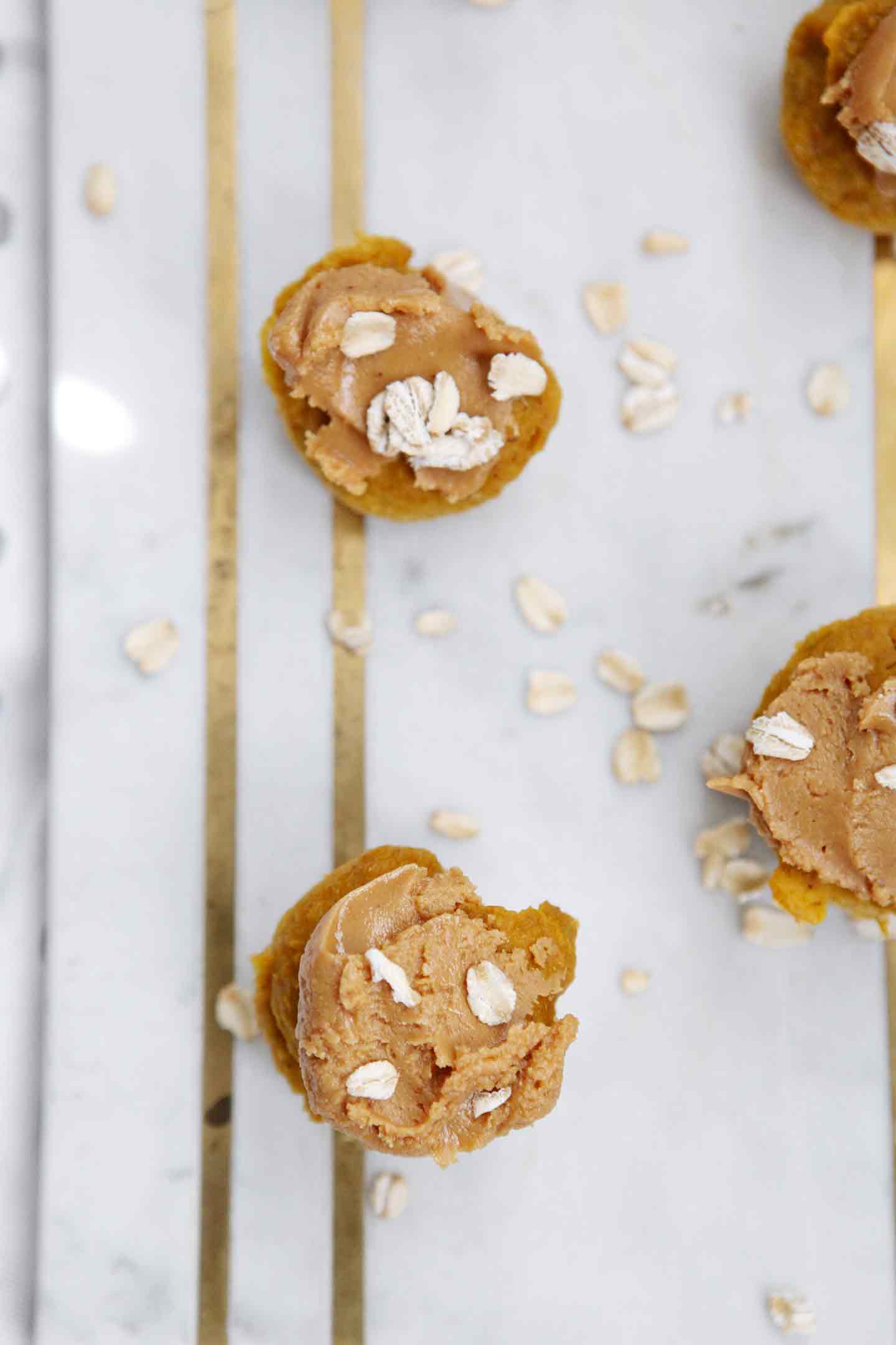 Overhead of homemade pupcake recipe, frosted with extra peanut butter, on a marble slab with oats sprinkled around them