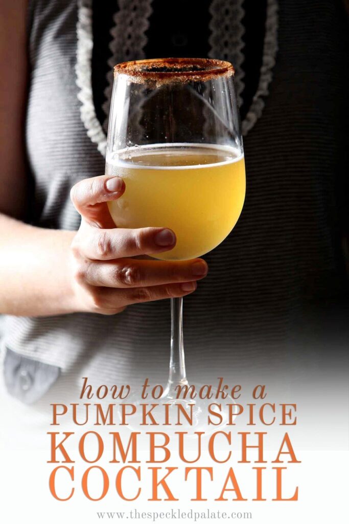 A woman holds a kombucha cocktail in a wine glass with the text 'how to make a pumpkin spice kombucha cocktail'