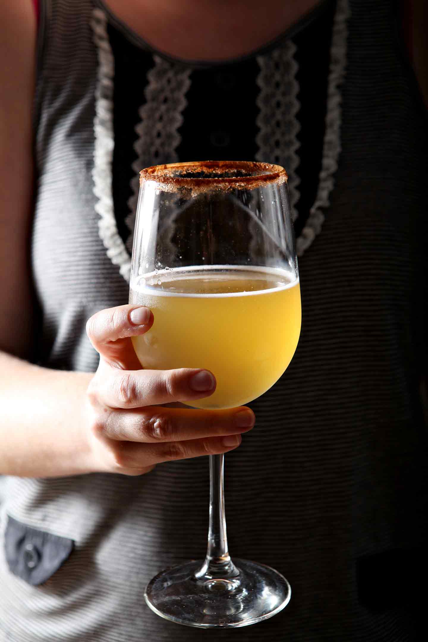 A woman holds a kombucha cocktail in a wine glass