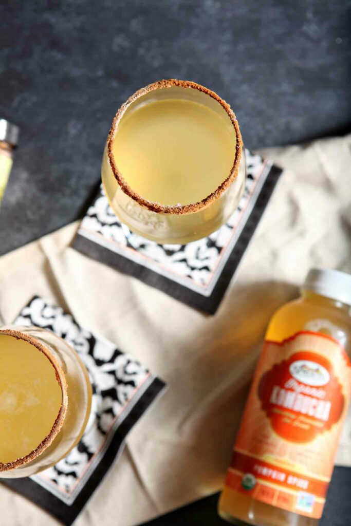 Overhead of two kombucha cocktails on a black table sitting next to a bottle of kombucha