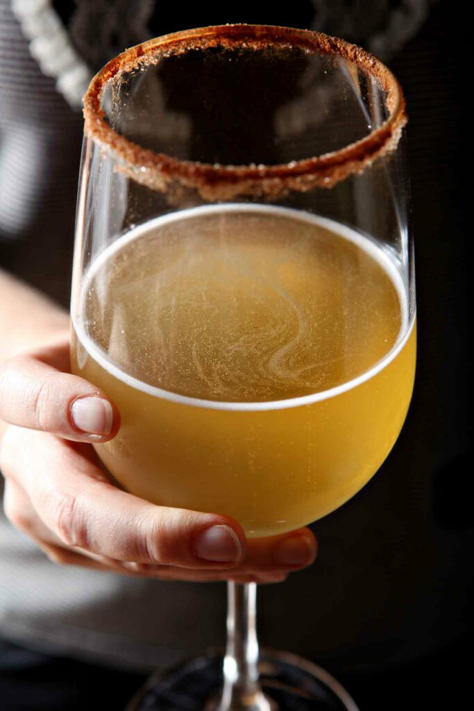 Close up of a woman holding a kombucha cocktail in a wine glass