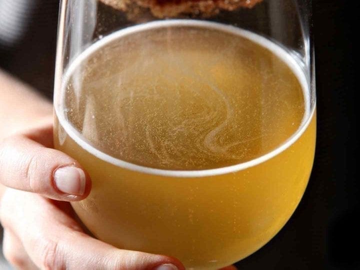 Close up of a woman holding a kombucha cocktail in a wine glass