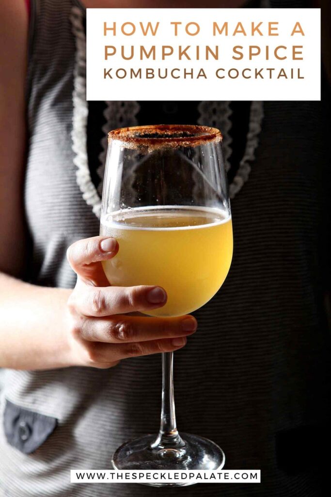 A woman holds a kombucha cocktail in a wine glass with the text 'how to make a pumpkin spice kombucha cocktail'