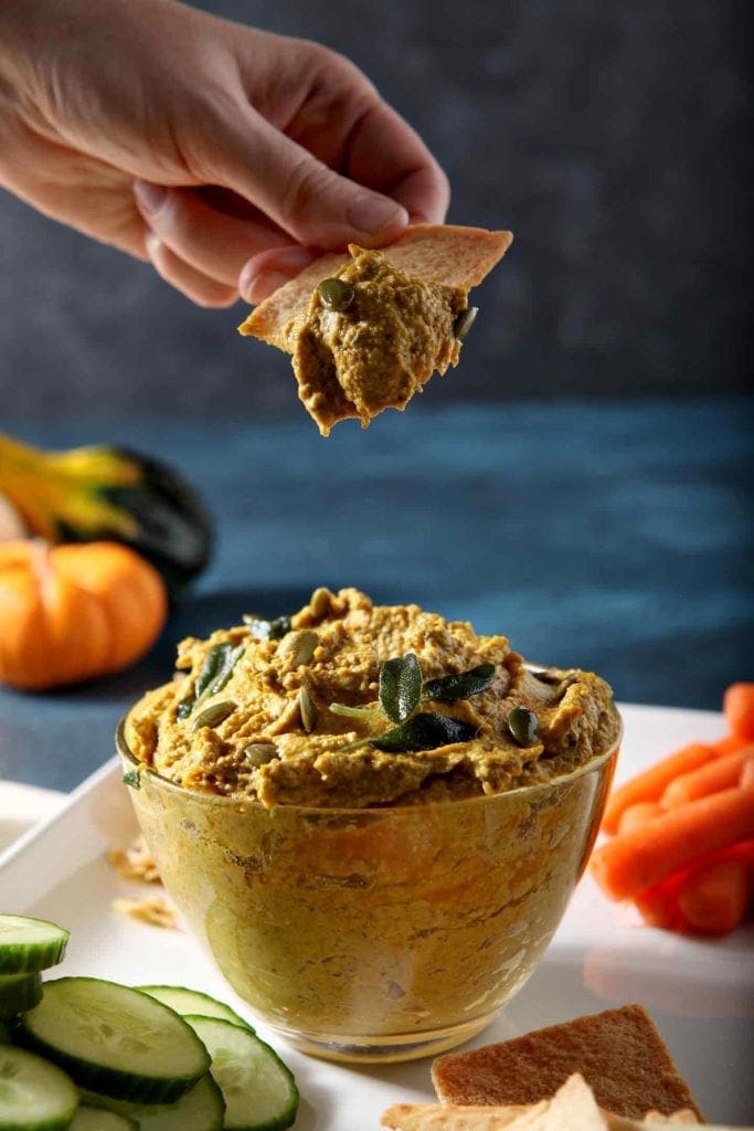 A person scoops a bite of Sage Pumpkin Hummus with a pita chip