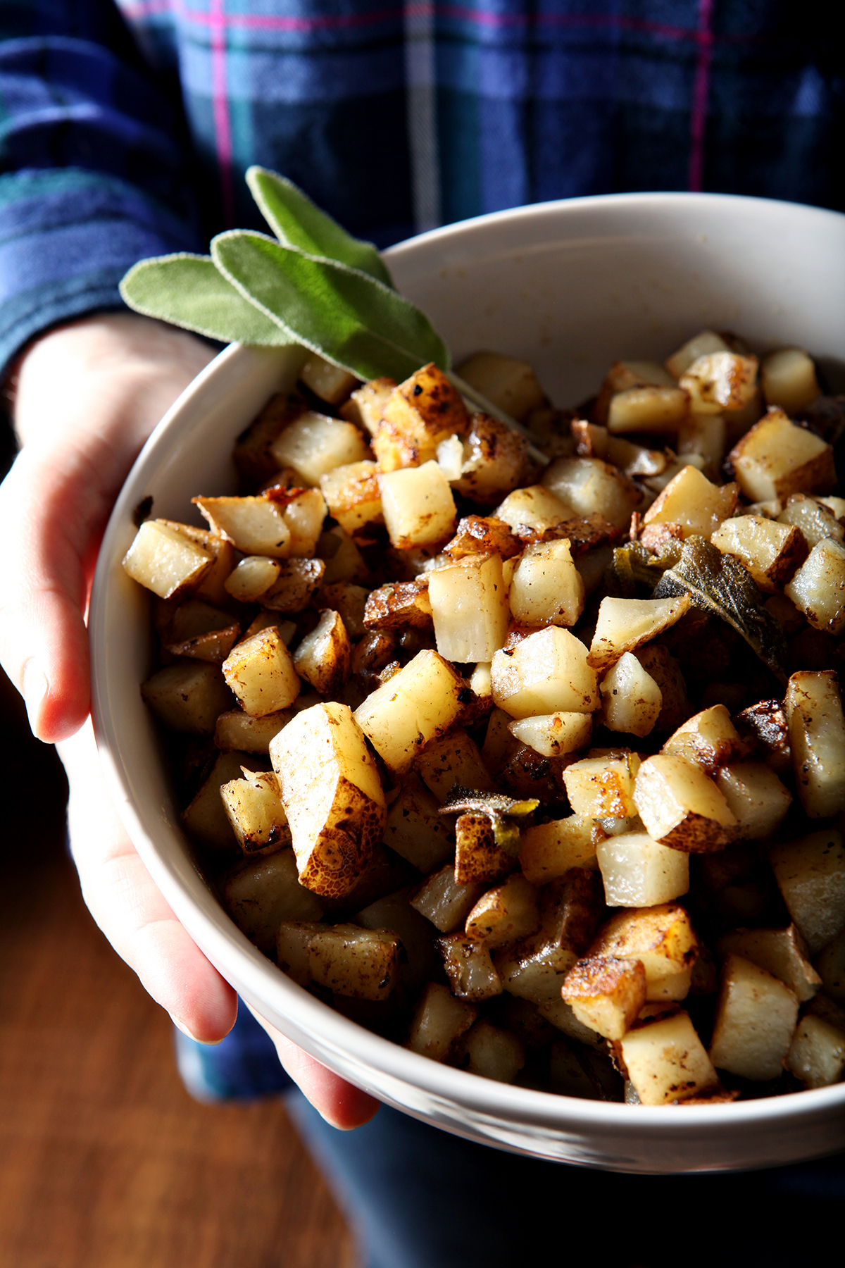 A woman in a blue and purple flannel shirt holds a bowl of sage home fries