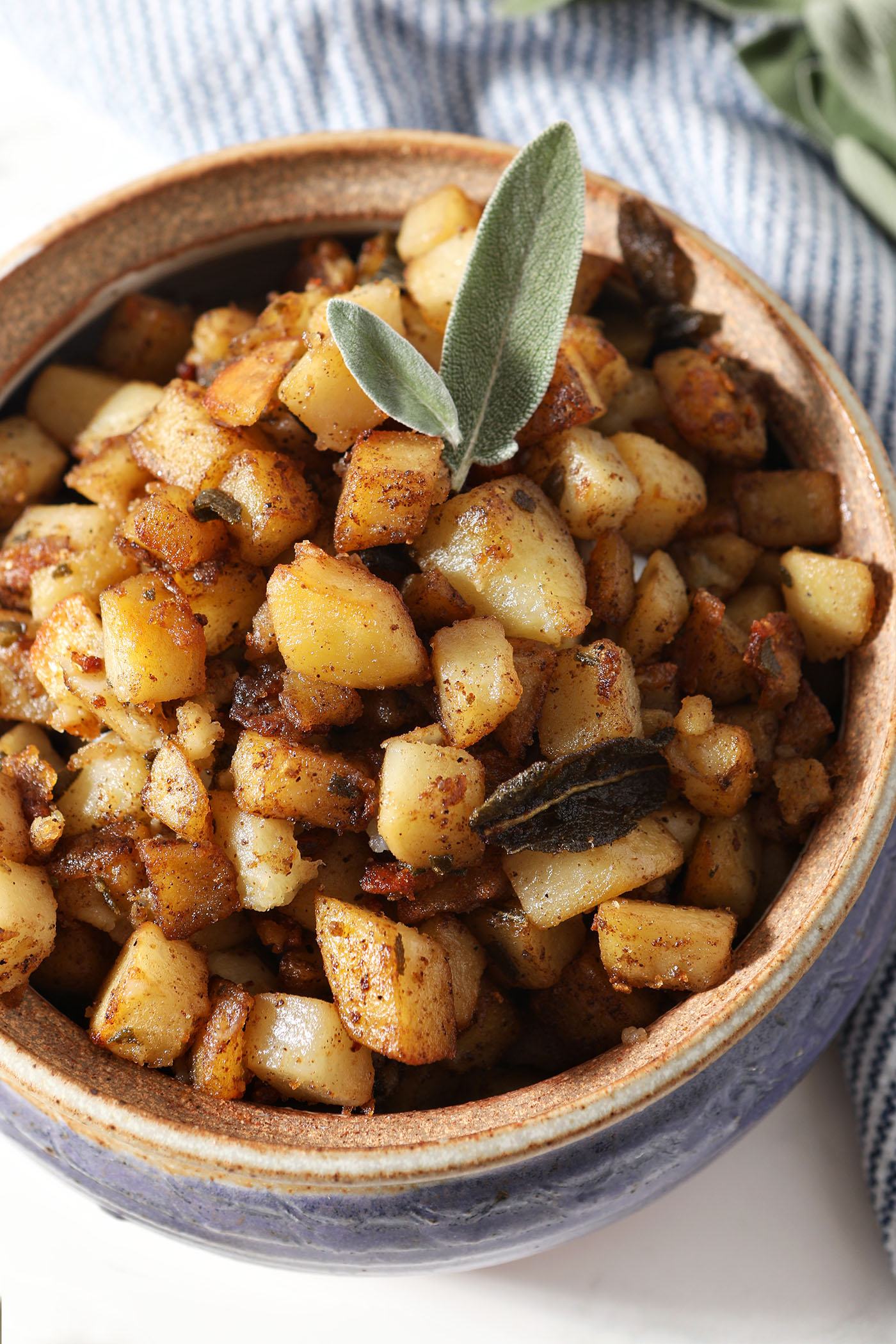 Overhead close-up image of home fries garnished with fresh and fried sage leaves