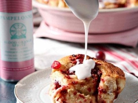 spoon drizzling frosting on a cinnamon roll
