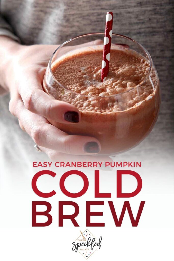 A woman holds a cold brew coffee drink in a glass with a red polka dot straw in her hand with the text 'easy cranberry pumpkin cold brew'