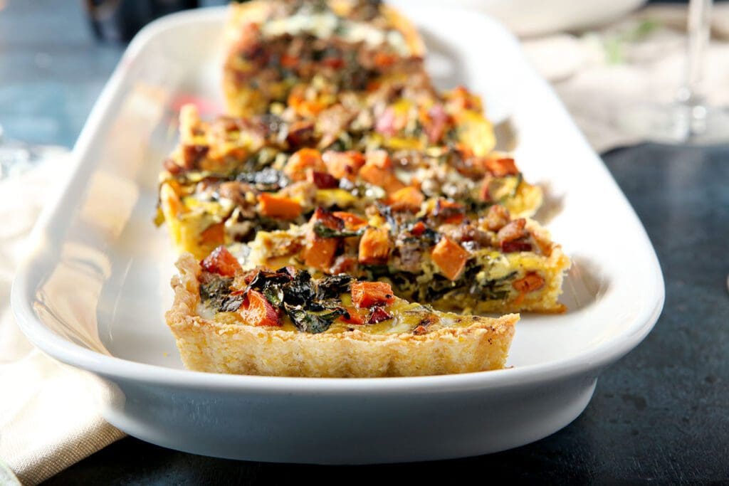 Sliced sweet potato quiche with sausage and collards on a white platter