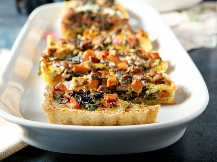 Sliced sweet potato quiche with sausage and collards on a white platter