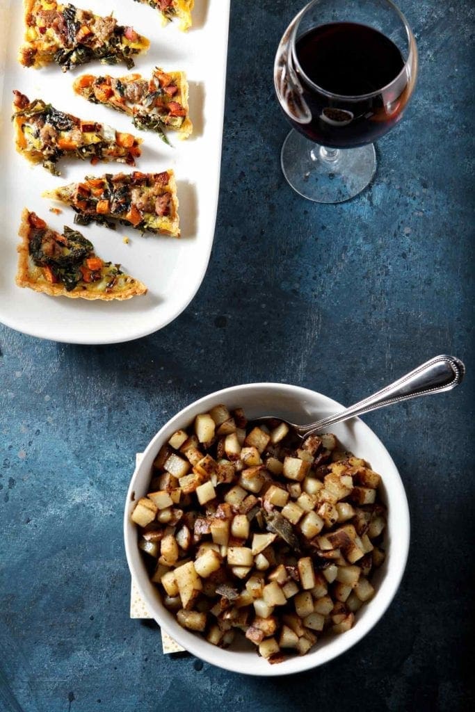 home fries and quiche on a blue table with wine